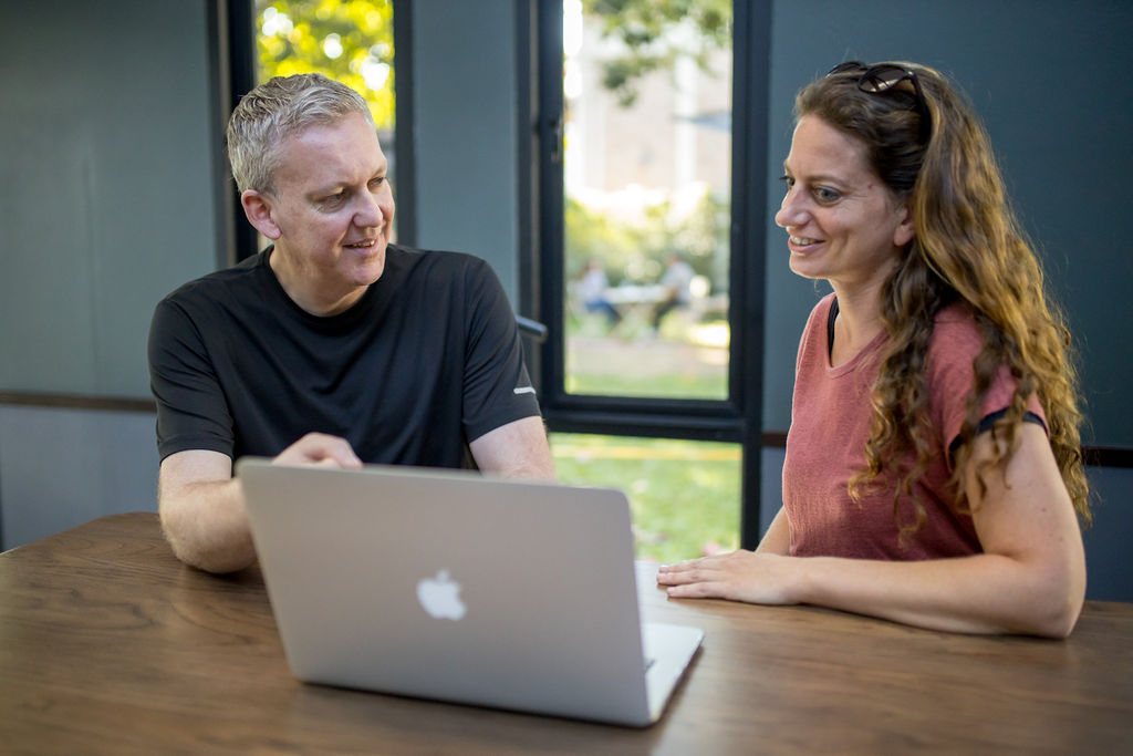 Stu Jordan at a table with a laptop, talking something through with a woman beside him